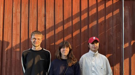 tre filmskapare framför faluröd stugvägg