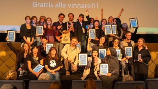 Glada människor på scen med priser, blommor och diplom.