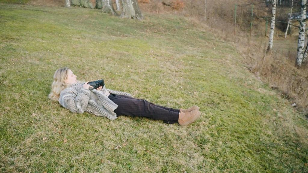 Kvinna med filmkamera ligger på gräsmatta och filmar