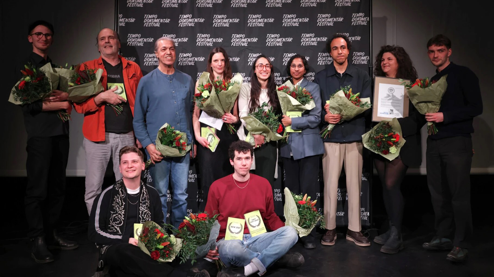 Ett stort gäng glada människor med diplom och blomsterbuketter.