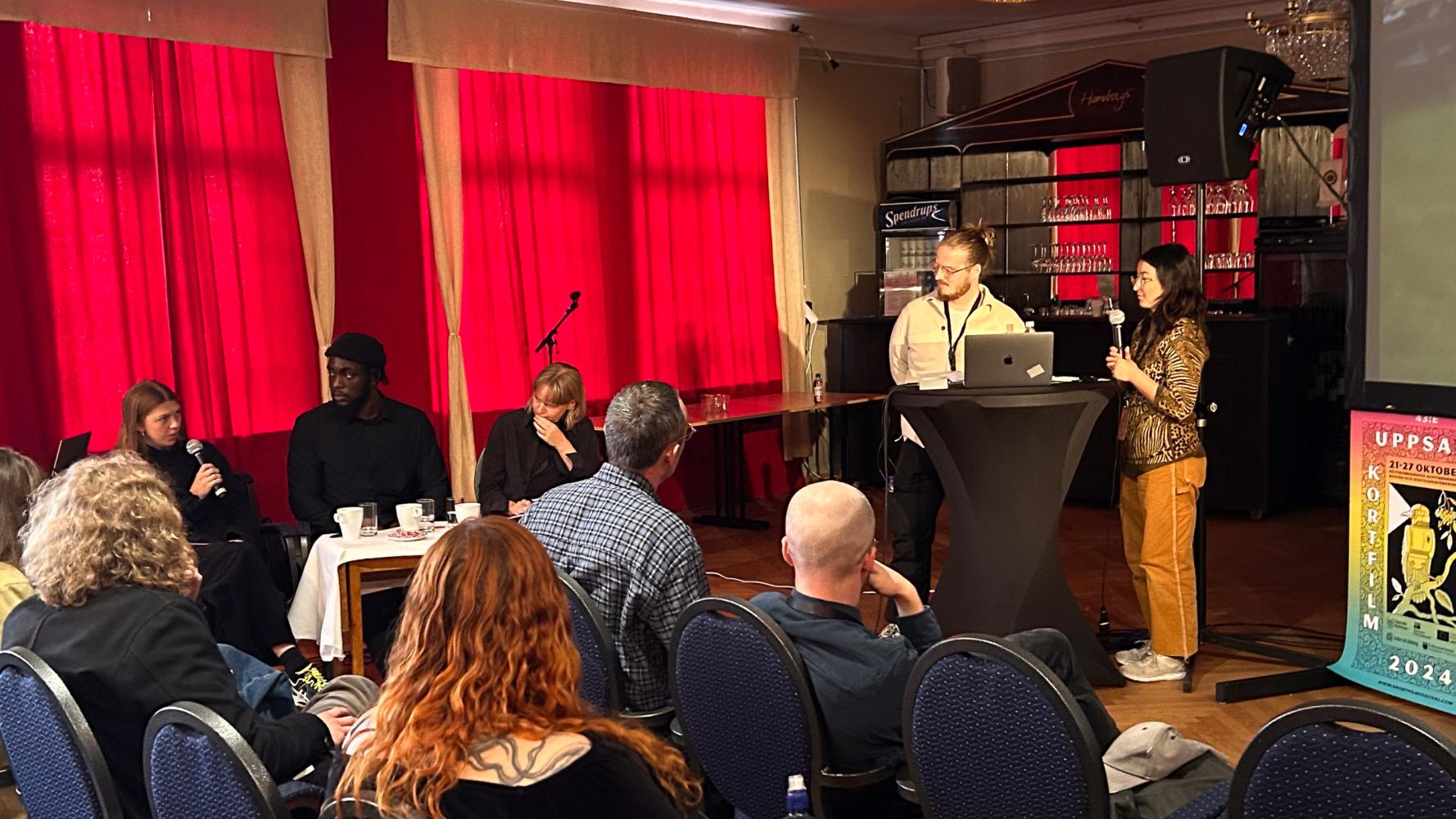 två personer presenterar inför publik och jury